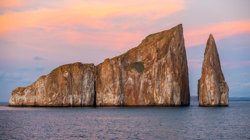 The volcanic rock formation of Kicker Rock (Leon Dormido) at sunset in the Pacific Ocean with sea birds silhouettes flying above the landmark, San Cristobal